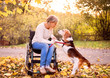 A senior woman in wheelchair with dog in autumn nature.